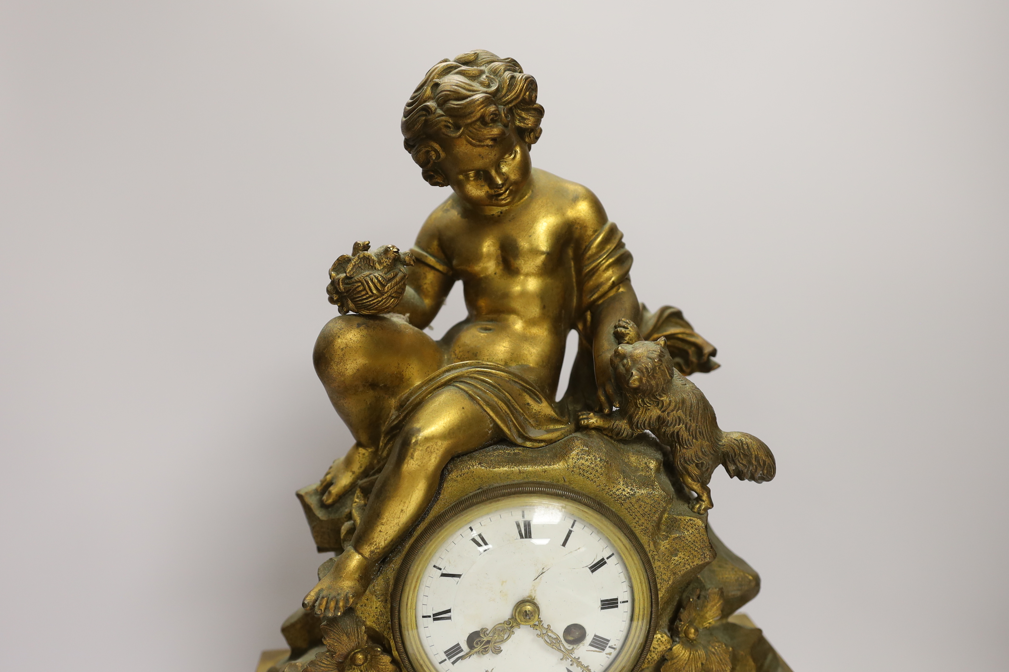 A decorative French ormolu mantel clock, the top a child playing with a kitten and the base with scrolled feet below a swag of flowers, 42cm high